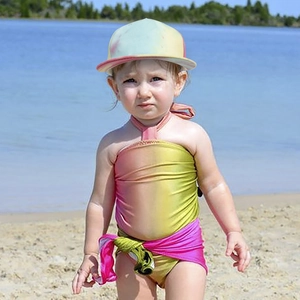 Outdoor view of gradient tie-dye sun hat and matching girls' one-piece swimsuit on the beach