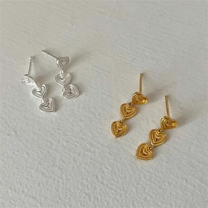 Macro detail of triple heart-shaped layered drop earrings in silver and gold finishes
