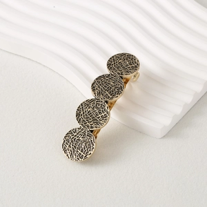 Close-up of golden vintage hair clip featuring textured circular metal disks on a white surface