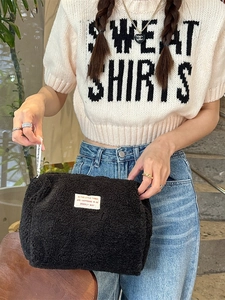 Large black fleece cosmetic bag with white text patch held by model in casual setting