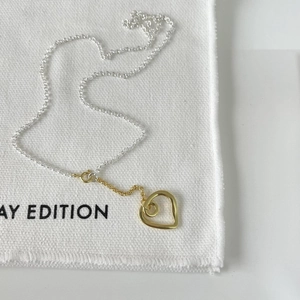 Detail of silver and gold bicolor chain necklace with hollow heart pendant on fabric