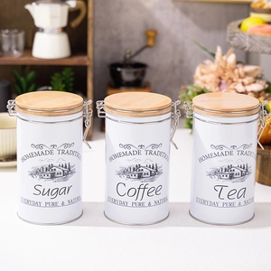 Three white tin canisters for sugar coffee and tea with wooden lids in a kitchen setting