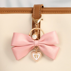 Pink satin ribbon bow bag charm with gold heart pendant and pearl detail on a beige bag