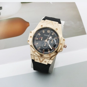Detail of gold alloy watch case and black silicone strap on a minimalist white stand