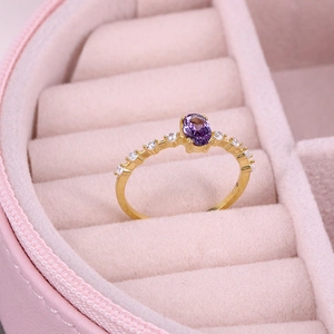 Detailed macro view of a gold ring with oval purple gemstone in a pink velvet box