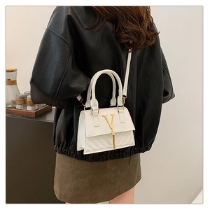 Detail of white quilted crossbody bag with golden V-buckle on a stylish model