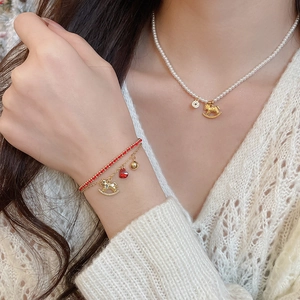 Detail of red braided bracelet and pearl necklace set with golden pony and heart charms