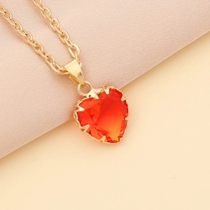 Macro shot of gold chain necklace featuring a red heart-shaped gemstone pendant