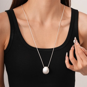 Detail view of long matte silver oval bean pendant necklace on a black tank top