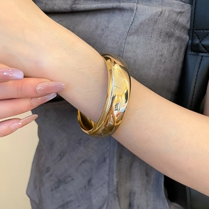 Gros plan d'un large bracelet manchette en métal doré poli avec finition miroir au poignet
