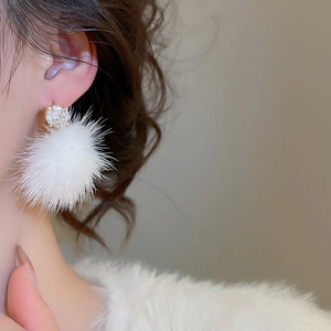 Détail de la boucle d'oreille pompon blanc avec zircon brillant portée par mannequin