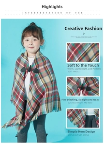 Detail of red and green plaid kids poncho with toggle buttons and fringe hemline