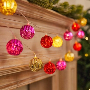 Colorful LED globe string lights with red pink and gold ornaments on a wooden fireplace