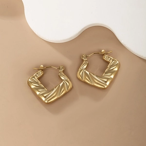 Detail of square gold hoop earrings with unique wrinkled texture on warm background