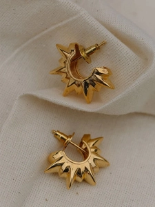 Macro shot of vintage 18K gold sunburst C-shaped earrings on a white textured fabric base