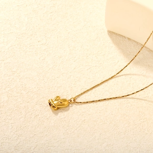 18K gold Christmas glove pendant necklace on minimalist textured background