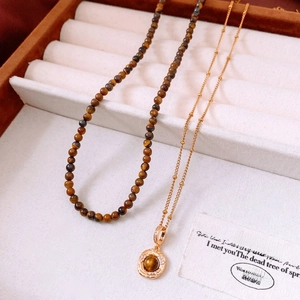 Detailed close-up of Tiger Eye stone pendant and beaded necklace in a beige jewelry box