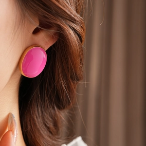 Close-up of a pink oval vintage earring with gold trim worn by a model in soft light