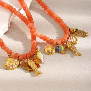 Detail of beaded necklace with 18K gold fish, shell, and octopus charms on stone surface