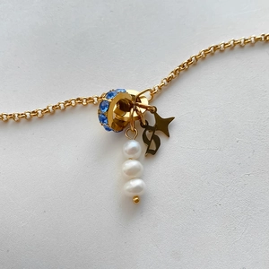 Macro view of gold jewelry charms featuring white pearls and blue rhinestone bead detail.