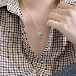 Silver coin pendant necklace worn by model wearing a brown checkered shirt