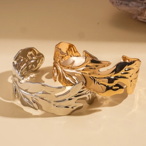 Minimalist metallic leaf open cuff bangles in gold and silver finish on warm background