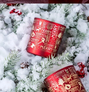 Detail eines roten Weihnachtskerzenhalters mit goldenen Rentier- und Baummotiven im Schnee