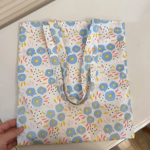 Detail shot of a canvas tote bag featuring a floral print with blue flowers on white fabric