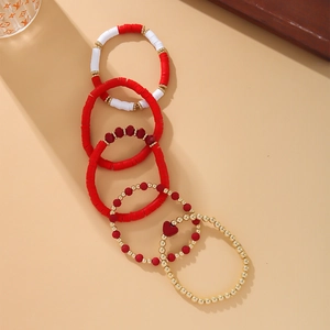 Detail shot of five stacked bohemian clay bracelets with gold beads and a red heart charm