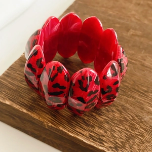Detail of red and black leopard print oval linked resin bracelet on a wooden stand