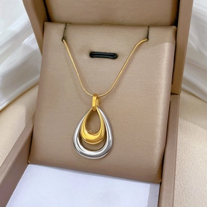 Macro detail of a minimalist double-layer teardrop pendant on a gold snake chain necklace