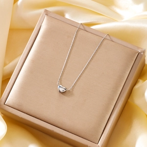 Close-up of a silver heart pendant necklace on silk fabric, showing refined metallic luster
