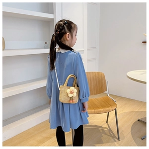 Girl wearing a beige straw bag with a yellow flower and orange pompom detail