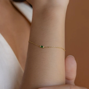 Detail of a gold stainless steel chain bracelet featuring a green emerald-cut zircon