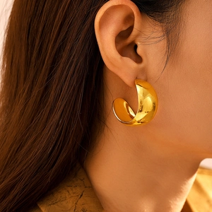 Polished gold PVD coated stainless steel C-shaped chunky hoop earrings worn by a model