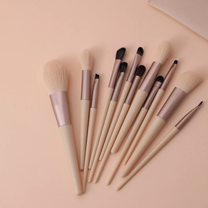 Flat lay view of 13 Morandi beige makeup brushes with rose gold ferrules on pink background