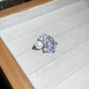 Detail of a sparkling zircon star earring with a white pearl in a beige velvet jewelry box