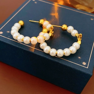 Close-up of C-shaped earrings with white pearls and gold beads on a blue jewelry box