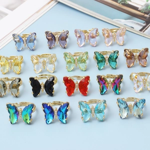 Set of 16 colorful crystal butterfly rings with golden bands on a light blue surface