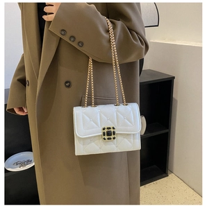 Close-up of heart-quilted white faux leather crossbody bag with golden chain and jewel buckle