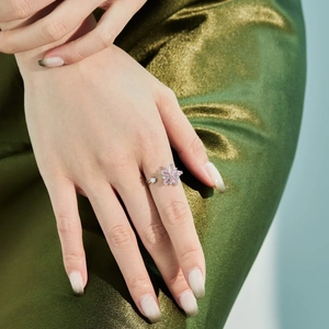 Detail shot of a pink floral rotating ring with crystals on green silk fabric