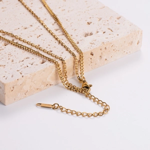 Minimalist gold chain necklace with bar pendant displayed on a beige stone platform