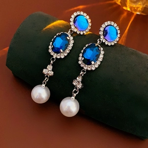 Dettaglio di orecchini vintage con gemme blu profondo e una perla bianca pendente