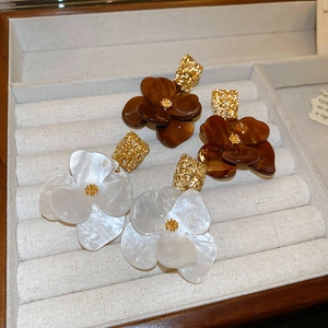 Detailed view of floral resin earrings in white and brown with golden stud accents