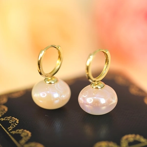 Macro shot of gold hoop earrings with iridescent pearl pendants against a floral background