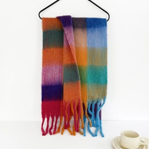 Detail of colorful plaid mohair scarf with tassels hanging near a coffee cup