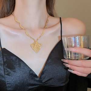 Close-up of golden fan-shaped necklace with embossed texture worn by a model