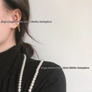 Detail of gold-plated non-pierced ear cuff with a dangling chain on a female model
