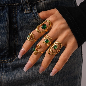 Detail of gold stacked rings with emerald green stones on model against denim fabric