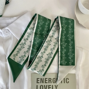 Close-up of a floral green silk twilly ribbon on a white shirt background with props